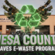 A viral, hyper-realistic YouTube thumbnail with a bold environmental tech atmosphere. The background is the Mesa County Hazardous Waste Facility exterior at golden hour with recycling trucks and stacked electronics visible through open bay doors, warm Colorado sunset lighting. The composition uses a dramatic low-angle shot to focus on the main subject: a massive glowing green recycling symbol made of circuit boards and crushed electronics rising like a phoenix. The image features massive 3D typography with strict hierarchy: The Primary Text reads exactly: 'MESA COUNTY'. This text is massive, the largest element in the frame, rendered in brushed aluminum chrome with electric green edge lighting to look like a high-budget 3D render. The Secondary Text reads exactly: 'SAVES E-WASTE PROGRAM'. This text is significantly smaller, positioned below the main text with thick white glow outline and subtle circuit trace effects to contrast against the background. Make sure text 2 is always different theme, style, effect and border compared to text 1. The text materials correspond to the story's concept. Crucial Instruction: There is absolutely NO other text, numbers, watermarks, or subtitles in this image other than these two specific lines. 8k, Unreal Engine 5, cinematic render