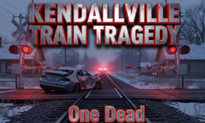 A viral, hyper-realistic YouTube thumbnail with a somber, tragic atmosphere. The background is a snow-dusted small-town railroad crossing in Kendallville, Indiana at dusk with red flashing signals and lowered gates. The composition uses a dramatic low-angle shot looking down the tracks toward a twisted, mangled silver car pushed off to the side, emergency lights flashing in the distance. The image features massive 3D typography with strict hierarchy: The Primary Text reads exactly: 'KENDALLVILLE TRAIN TRAGEDY'. This text is massive, the largest element in the frame, rendered in cold brushed steel with glowing red edges to look like a high-budget 3D render. The Secondary Text reads exactly: 'One Dead'. This text is significantly smaller, positioned below the main text with a thick white outline and subtle red glow border to stand out sharply against the dark scene. The text materials correspond to the story's concept. Crucial Instruction: There is absolutely NO other text, numbers, watermarks, or subtitles in this image other than these two specific lines. 8k, Unreal Engine 5, cinematic render