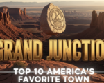 A viral, hyper-realistic YouTube thumbnail with a warm Western American adventure atmosphere. The background is a dramatic Colorado National Monument canyon at golden hour with deep red rock formations and the Grand Junction skyline faintly visible in the valley below. The composition uses a low-angle heroic shot to focus on the main subject: a massive polished granite stone engraved with the city seal floating above the canyon rim. The image features massive 3D typography with strict hierarchy: The Primary Text reads exactly: 'GRAND JUNCTION'. This text is massive, the largest element in the frame, rendered in molten sunset gold chrome to look like a high-budget 3D render. The Secondary Text reads exactly: 'TOP 10 AMERICA'S FAVORITE TOWN'. This text is significantly smaller, positioned below the main text with a thick white glow border and subtle lens flare effect. Make sure text 2 has completely different style and border compared to text 1. The text materials correspond to the story's concept. Crucial Instruction: There is absolutely NO other text, numbers, watermarks, or subtitles in this image other than these two specific lines. 8k, Unreal Engine 5, cinematic render