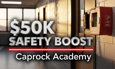 A viral, hyper-realistic YouTube thumbnail with a serious protective atmosphere. The background is a modern school hallway in Grand Junction Colorado at golden hour with warm sunlight streaming through new safety windows. The composition uses a dramatic low-angle shot to focus on the main subject: a sleek black two-way radio and a red AED unit mounted on the wall beside a classroom door with fresh one-way privacy film. The image features massive 3D typography with strict hierarchy: The Primary Text reads exactly: '$50K SAFETY BOOST'. This text is massive, the largest element in the frame, rendered in brushed steel chrome to look like a high-budget 3D render. The Secondary Text reads exactly: 'Caprock Academy'. This text is significantly smaller, positioned below the main text. It features a thick, glowing red border/outline to contrast against the background. Make sure text 2 is always different theme, style, effect and border compared to text 1. The text materials correspond to the story's concept. Crucial Instruction: There is absolutely NO other text, numbers, watermarks, or subtitles in this image other than these two specific lines. 8k, Unreal Engine 5, cinematic render
