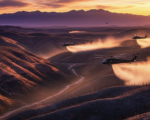 A viral, hyper-realistic YouTube thumbnail with a dramatic western wildfire recovery atmosphere. The background is a vast blackened Colorado landscape at golden hour with massive helicopters kicking up dust while dropping seed over steep burn scars, distant purple mountains under a fiery sunset sky. The composition uses a low-angle cinematic shot to focus on the main subject: a huge spinning helicopter rotor blade in sharp detail. The image features massive 3D typography with strict hierarchy: The Primary Text reads exactly: 'COLORADO FIGHTS BACK'. This text is massive, the largest element in the frame, rendered in molten orange chrome with glowing embers flying off the letters like real fire particles. The Secondary Text reads exactly: '265,000 Acres Rising'. This text is significantly smaller, positioned below the main text with a thick white outline and red glow border to pop against the dark terrain. 8k, Unreal Engine 5, cinematic render.