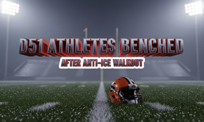 A viral, hyper-realistic YouTube thumbnail with a tense, red-and-blue-lit stadium atmosphere. The background is a dark Western Colorado Friday night football field under floodlights with empty bleachers and a cold mist rolling in. The composition uses a dramatic low angle to focus on the main subject: a lone orange-and-black football helmet sitting abandoned on the 50-yard line, dew on the grass, stadium lights casting long shadows. The image features massive 3D typography with strict hierarchy: The Primary Text reads exactly: 'D51 ATHLETES BENCHED'. This text is massive, the largest element in the frame, rendered in cold chrome metal with glowing red edges like heated steel. The Secondary Text reads exactly: 'AFTER ANTI-ICE WALKOUT'. This text is significantly smaller, positioned below the main text with a thick white outline and black sticker-style border to pop against the dark field. 8k, Unreal Engine 5, cinematic render