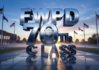 A viral, hyper-realistic YouTube thumbnail with a powerful law-enforcement atmosphere. The background is the Fort Wayne Public Safety Academy at dawn with soft blue sunrise light cutting through morning mist and rows of American flags waving. The composition uses a dramatic low-angle shot to focus on the main subject: a gleaming silver police badge floating forward in mid-air with perfect reflection. The image features massive 3D typography with strict hierarchy: The Primary Text reads exactly: 'FWPD 70TH CLASS'. This text is massive, the largest element in the frame, rendered in polished chrome with realistic depth and edge lighting to look like a high-budget 3D render. The Secondary Text reads exactly: 'BEGINS NOW'. This text is significantly smaller, positioned below the main text with a bold red outline and subtle glow effect to contrast against the background. Make sure text 2 is always different theme, style, effect and border compared to text 1. The text materials correspond to the story's concept. Crucial Instruction: There is absolutely NO other text, numbers, watermarks, or subtitles in this image other than these two specific lines. 8k, Unreal Engine 5, cinematic render