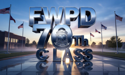 A viral, hyper-realistic YouTube thumbnail with a powerful law-enforcement atmosphere. The background is the Fort Wayne Public Safety Academy at dawn with soft blue sunrise light cutting through morning mist and rows of American flags waving. The composition uses a dramatic low-angle shot to focus on the main subject: a gleaming silver police badge floating forward in mid-air with perfect reflection. The image features massive 3D typography with strict hierarchy: The Primary Text reads exactly: 'FWPD 70TH CLASS'. This text is massive, the largest element in the frame, rendered in polished chrome with realistic depth and edge lighting to look like a high-budget 3D render. The Secondary Text reads exactly: 'BEGINS NOW'. This text is significantly smaller, positioned below the main text with a bold red outline and subtle glow effect to contrast against the background. Make sure text 2 is always different theme, style, effect and border compared to text 1. The text materials correspond to the story's concept. Crucial Instruction: There is absolutely NO other text, numbers, watermarks, or subtitles in this image other than these two specific lines. 8k, Unreal Engine 5, cinematic render