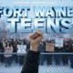 A viral, hyper-realistic YouTube thumbnail with a tense, defiant activist atmosphere. The background is a cold February morning outside South Side High School in Fort Wayne, chain-link fence in foreground, hundreds of diverse teens holding hand-made signs, light snow falling. The composition uses a dramatic low-angle shot to focus on the main subject: a raised fist gripping a bold protest sign on wooden stick. The image features massive 3D typography with strict hierarchy: The Primary Text reads exactly: 'FORT WAYNE TEENS'. This text is massive, the largest element in the frame, rendered in frozen ice-blue chrome with cracking ice effect to look like a high-budget 3D render. The Secondary Text reads exactly: 'DEFY ICE'. This text is significantly smaller, positioned below the main text. It features a thick, glowing red border/outline (sticker style) to contrast against the cold background. Make sure text 2 is always different theme, style, effect and border compared to text 1. The text materials correspond to the story's concept. Crucial Instruction: There is absolutely NO other text, numbers, watermarks, or subtitles in this image other than these two specific lines. 8k, Unreal Engine 5, cinematic render.