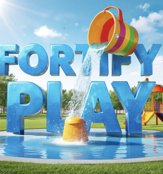 A viral, hyper-realistic YouTube thumbnail with a bright, summer community vibe atmosphere. The background is a sunny, green park environment with a modern splash pad and playground equipment under a clear blue sky with warm sunlight. The composition uses a low angle to focus on the main subject: a colorful, 3D-rendered bucket dumping water (from a splash pad feature). The image features massive 3D typography with strict hierarchy: The Primary Text reads exactly: 'FORTIFY PLAY'. This text is massive, the largest element in the frame, rendered in glossy blue water texture to look like a high-budget 3D render. The Secondary Text reads exactly: '$1.5M GOAL'. This text is significantly smaller, positioned below the main text. It features a thick, distinct white border/outline (sticker style) to contrast against the background. Make sure text 2 is always different theme, style, effect and border compared to text 1.