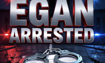 A viral, hyper-realistic YouTube thumbnail with a tense crime-news atmosphere. The background is a dark Mesa County courthouse at night with red and blue police lights flashing across wet pavement and barbed wire in the foreground. The composition uses a dramatic low-angle shot to focus on the main subject: a pair of steel handcuffs locked around a cracked protection order document. The image features massive 3D typography with strict hierarchy: The Primary Text reads exactly: 'EGAN ARRESTED AGAIN'. This text is massive, the largest element in the frame, rendered in cold chrome metal with glowing red edges to look like a high-budget 3D render. The Secondary Text reads exactly: 'Protection Order Breach'. This text is significantly smaller, positioned below the main text. It features a thick white border with red outline sticker style to contrast against the dark background. Make sure text 2 is always different theme, style, effect and border compared to text 1. The text materials correspond to the story's concept. Crucial Instruction: There is absolutely NO other text, numbers, watermarks, or subtitles in this image other than these two specific lines. 8k, Unreal Engine 5, cinematic render