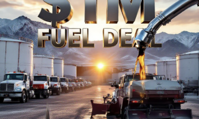 A viral, hyper-realistic YouTube thumbnail with a gritty industrial Colorado atmosphere. The background is a massive fuel storage yard at golden hour with rugged Mesa County mountains behind, warm sunlight glinting off white and red bulk tanks, dust in the air, county trucks lined up. The composition uses a dramatic low-angle shot to focus on the main subject: a gleaming chrome fuel nozzle dramatically dripping diesel into a county snowplow tank. Image size should be 3:2. The image features massive 3D typography with strict hierarchy: The Primary Text reads exactly: '$1M FUEL DEAL'. This text is massive, the largest element in the frame, rendered in polished chrome with realistic liquid diesel dripping effects to look like a high-budget 3D render. The Secondary Text reads exactly: 'MESA COUNTY SAVES'. This text is significantly smaller, positioned below the main text. It features a thick orange safety-striped border to contrast against the background. 8k, Unreal Engine 5, cinematic render