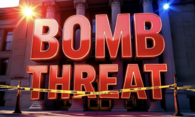 A viral, hyper-realistic YouTube thumbnail with a tense crime-scene atmosphere. The background is the Dennis Maes Judicial Building in Pueblo under harsh afternoon sunlight with red and blue emergency lights flashing across the facade. The composition uses a dramatic low angle to focus on the main subject: a large abandoned courthouse entrance with yellow police tape stretched across the doors. Image size should be 3:2. The image features massive 3D typography with strict hierarchy: The Primary Text reads exactly: 'BOMB THREAT'. This text is massive, the largest element in the frame, rendered in glowing red chrome to look like a high-budget 3D render. The Secondary Text reads exactly: 'Pueblo Courthouse Evacuated'. This text is significantly smaller, positioned below the main text. It features a thick white border with black outline (sticker style) to contrast against the background. Make sure text 2 is always different theme, style, effect and border compared to text 1.