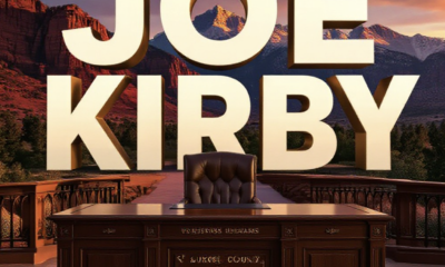 A viral, hyper-realistic YouTube thumbnail with a cinematic government authority atmosphere. The background is the dramatic red rock landscape of western Colorado at golden hour with the San Juan mountains glowing behind the historic Montrose County Courthouse. The composition uses a low-angle shot to focus on the main subject: a polished wooden county manager's desk with an engraved nameplate facing forward. Image size should be 3:2. The image features massive 3D typography with strict hierarchy: The Primary Text reads exactly: 'JOE KIRBY'. This text is massive, the largest element in the frame, rendered in brushed bronze metal with realistic light reflections to look like a high-budget 3D render. The Secondary Text reads exactly: 'RETURNS TO MONTROSE'. This text is significantly smaller, positioned below the main text. It features a thick white border with red outline in sticker style to contrast against the mountain background. Make sure text 2 is always different theme, style, effect and border compared to text 1