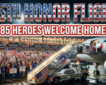 A viral, hyper-realistic YouTube thumbnail with a patriotic, heartfelt American atmosphere. The background is a packed Fort Wayne airport terminal at night filled with hundreds of people waving American flags under warm terminal lights and red-white-blue buntings. The composition uses a dramatic low-angle shot to focus on the main subject: a gleaming silver airline jet stair truck with the Honor Flight logo. Image size should be 3:2. The image features massive 3D typography with strict hierarchy: The Primary Text reads exactly: '55TH HONOR FLIGHT'. This text is massive, the largest element in the frame, rendered in polished chrome with subtle American flag reflections to look like a high-budget 3D render. The Secondary Text reads exactly: '85 HEROES WELCOME HOME'. This text is significantly smaller, positioned below the main text. It features a thick white glow border with red outline (sticker style) to contrast against the background. Make sure text 2 is always different theme, style, effect and border compared to text 1