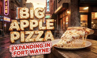 A viral, hyper-realistic YouTube thumbnail with a warm, inviting foodie atmosphere. The background is a bustling urban street corner at golden hour with glowing neon signs reflecting off rain-kissed asphalt and a cozy brick storefront with warm interior light spilling out. The composition uses a low angle to focus on the main subject: a massive, steaming New York-style pizza slice on a classic paper plate, cheese stretching dramatically, sitting on a rustic wooden counter with no human faces visible. Image size should be 3:2. The image features massive 3D typography with strict hierarchy: The Primary Text reads exactly: 'BIG APPLE PIZZA'. This text is massive, the largest element in the frame, rendered in molten mozzarella cheese with golden crispy crust edges to look like a high-budget 3D render. The Secondary Text reads exactly: 'EXPANDING IN FORT WAYNE'. This text is significantly smaller, positioned below the main text. It features a thick red and white checkered border outline in a retro diner sticker style to contrast against the warm background. The text materials correspond to the story's concept. Crucial Instruction: There is absolutely NO other text, numbers, watermarks, or subtitles in this image other than these two specific lines. 8k, Unreal Engine 5, cinematic render.