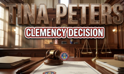 A viral, hyper-realistic YouTube thumbnail with a Government/Legal atmosphere. The background is a Colorado state capitol building interior with dramatic courtroom lighting, featuring rich mahogany wood panels and morning sunlight streaming through tall windows. The composition uses a Low Angle shot to focus on the main subject: a highly detailed wooden judge's gavel resting on an official clemency document with the Colorado state seal visible, surrounded by legal folders and an antique brass scale of justice slightly out of focus in the background. Image size should be 3:2. The image features massive 3D typography with strict hierarchy: The Primary Text reads exactly: 'TINA PETERS'. This text is massive, the largest element in the frame, rendered in Polished Bronze with Marble Veining to look like a high-budget 3D render with dramatic shadows. The Secondary Text reads exactly: 'CLEMENCY DECISION'. This text is significantly smaller, positioned below the main text. It features a thick, distinct red and white border/outline in sticker style to contrast against the background. Make sure text 2 is always different theme, style, effect and border compared to text 1. The text materials correspond to the story's legal and governmental concept. Crucial Instruction: There is absolutely NO other text, numbers, watermarks, or subtitles in this image other than these two specific lines. 8k, Unreal Engine 5, cinematic render