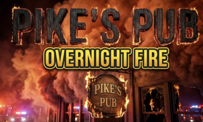 A viral, hyper-realistic YouTube thumbnail with a dramatic emergency atmosphere. The background is a nighttime commercial building exterior with billowing smoke clouds illuminated by red and orange emergency lights, creating an intense amber glow against the dark sky. The composition uses a low angle shot to focus on the main subject: a weathered wooden pub sign with flames licking at its edges, emergency vehicle lights reflecting off broken windows in the background. Image size should be 3:2. The image features massive 3D typography with strict hierarchy: The Primary Text reads exactly: 'PIKE'S PUB'. This text is massive, the largest element in the frame, rendered in charred wood texture with glowing ember edges to look like a high-budget 3D render. The Secondary Text reads exactly: 'OVERNIGHT FIRE'. This text is significantly smaller, positioned below the main text. It features a thick, distinct yellow and black border outline in bold sans-serif style to contrast against the smoky background. Make sure text 2 is always different theme, style, effect and border compared to text 1. The text materials correspond to the story's concept. Crucial Instruction: There is absolutely NO other text, numbers, watermarks, or subtitles in this image other than these two specific lines. 8k, Unreal Engine 5, cinematic render.
