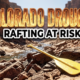 A viral, hyper-realistic YouTube thumbnail with a Kinetic atmosphere. The background is a sun-baked canyon riverbed with extremely low water levels with harsh midday sunlight. The composition uses a Low Angle to focus on the main subject: a bright yellow rubber rafting paddle resting on dry jagged rocks. Image size should be 3:2. The image features massive 3D typography with strict hierarchy: The Primary Text reads exactly: 'COLORADO DROUGHT'. This text is massive, the largest element in the frame, rendered in Orange and Yellow Fire to look like a high-budget 3D render. The Secondary Text reads exactly: 'RAFTING AT RISK'. This text is significantly smaller, positioned below or next to the main text. It features a thick, distinct black color border/outline (sticker style) to contrast against the background. Make sure text 2 is always different theme, style, effect and border compared to text 1. The text materials correspond to the story's concept. Crucial Instruction: There is absolutely NO other text, numbers, watermarks, or subtitles in this image other than these two specific lines. 8k, Unreal Engine 5, cinematic render
