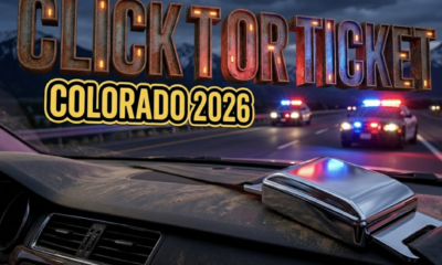 A viral, hyper-realistic YouTube thumbnail with a serious public safety atmosphere. The background is a Colorado highway patrol scene with red and blue emergency lights casting dramatic illumination across an evening mountain highway, with the Rockies visible in the distance. The composition uses a low angle shot to focus on the main subject: a chrome-plated seatbelt buckle in the foreground, gleaming under patrol car lights, positioned on a car dashboard. Image size should be 3:2. The image features massive 3D typography with strict hierarchy: The Primary Text reads exactly: 'CLICK IT OR TICKET'. This text is massive, the largest element in the frame, rendered in metallic chrome with red emergency light reflections to look like a high-budget 3D render. The Secondary Text reads exactly: 'COLORADO 2026'. This text is significantly smaller, positioned below the main text. It features a thick, distinct yellow and black border outline in sticker style to contrast against the background. Make sure text 2 is always different theme, style, effect and border compared to text 1. The text materials correspond to the story's concept. Crucial Instruction: There is absolutely NO other text, numbers, watermarks, or subtitles in this image other than these two specific lines. 8k, Unreal Engine 5, cinematic render