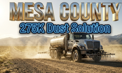 A viral, hyper-realistic YouTube thumbnail with a professional municipal infrastructure atmosphere. The background is a dusty Colorado dirt road stretching toward distant mountains with golden afternoon sunlight and swirling dust particles suspended in the air. The composition uses a low-angle camera perspective to focus on the main subject: a large metal road treatment tanker truck with magnesium chloride spraying equipment visible. The image features massive 3D typography with strict hierarchy: The Primary Text reads exactly: "MESA COUNTY". This text is massive, the largest element in the frame, rendered in shimmering chrome and metallic gold material to look like a high-budget 3D render with real-time reflections. The Secondary Text reads exactly: "275K Dust Solution". This text is significantly smaller, positioned below the primary text, featuring a thick bright blue neon border with a sticker-style outline that contrasts sharply against the dusty background. The text materials correspond to the professional infrastructure concept. Crucial Instruction: There is absolutely no other text, numbers, watermarks, or subtitles in this image other than these two specific lines. 8k, Unreal Engine 5, cinematic render.