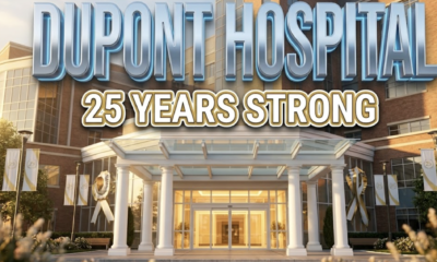 A viral, hyper-realistic YouTube thumbnail with a Healthcare Excellence atmosphere. The background is a modern hospital exterior with warm golden hour lighting cascading across glass windows and brick facade, creating an inspiring and trustworthy mood with soft bokeh effects in the foreground. The composition uses a Low Angle shot to focus on the main subject: a grand illuminated hospital entrance with pristine white columns, automatic doors reflecting warm interior light, and manicured landscaping with subtle anniversary celebration elements like elegant banners. Image size should be 3:2. The image features massive 3D typography with strict hierarchy: The Primary Text reads exactly: 'DUPONT HOSPITAL'. This text is massive, the largest element in the frame, rendered in Premium Medical Chrome with soft blue accent lighting to look like a high-budget 3D render with clean, professional aesthetic. The Secondary Text reads exactly: '25 YEARS STRONG'. This text is significantly smaller, positioned below the main text. It features a thick, distinct gold border with white fill (sticker style) to contrast against the background with a celebration ribbon effect. Make sure text 2 is always different theme, style, effect and border compared to text 1. The text materials correspond to the story's medical milestone concept. Crucial Instruction: There is absolutely NO other text, numbers, watermarks, or subtitles in this image other than these two specific lines. 8k, Unreal Engine 5, cinematic render.